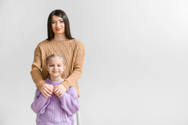 Маленька дівчинка і її мати в теплих светрах на світлому фоні
 - Фото, зображення