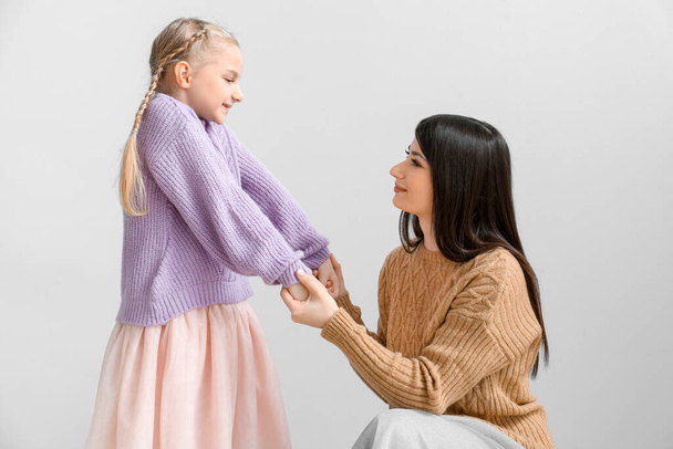 Little girl and her mother in warm sweaters holding hands on light background - Valokuva, kuva