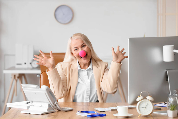 Забавная взрослая женщина с клоунским носом в офисе. Празднование Дня дураков - Фото, изображение