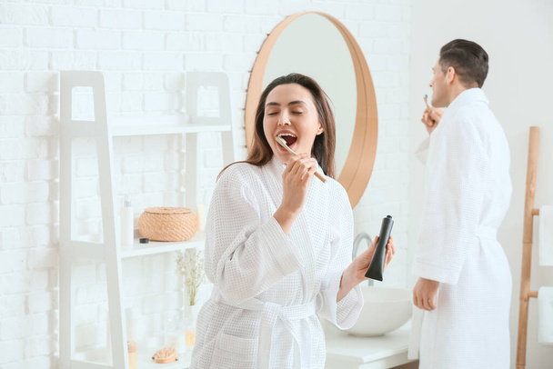 Jeune couple brossant les dents avec de la pâte à dents au charbon actif dans la salle de bain - Photo, image