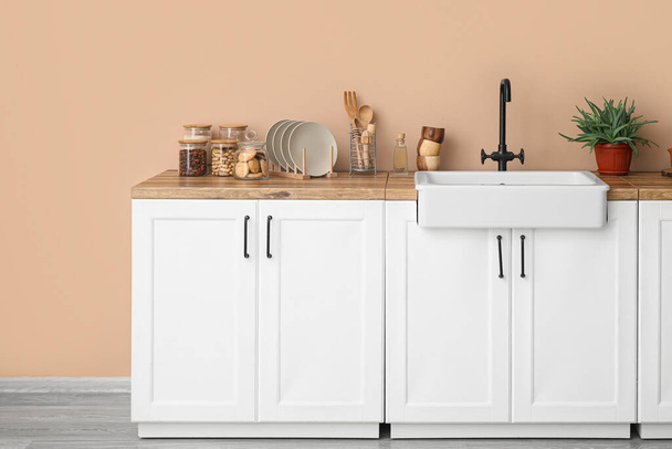 Counters with sink, houseplant and kitchen utensils near beige wall - Φωτογραφία, εικόνα