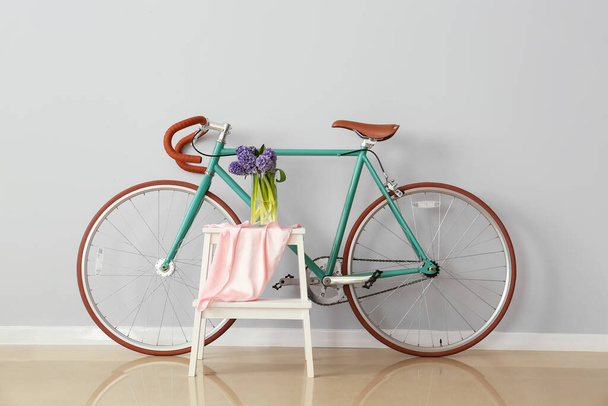 Vase with hyacinth flowers on stepladder stool and bicycle near light wall in room - Fotografie, Obrázek