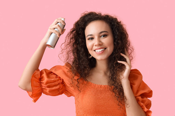 Pretty young African-American woman with hair spray on pink background - Foto, afbeelding