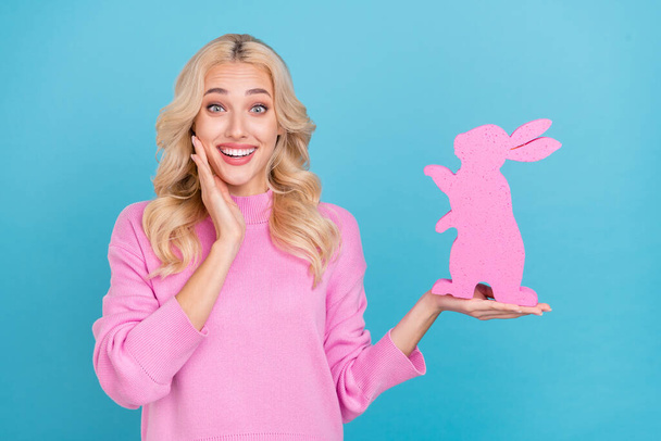 Portrait of attractive impressed cheerful wavy-haired girl holding hare figure isolated over bright blue color background - 写真・画像
