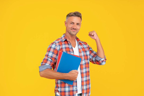 Excited guy teacher making winning gesture holding books yellow background, education - Foto, immagini
