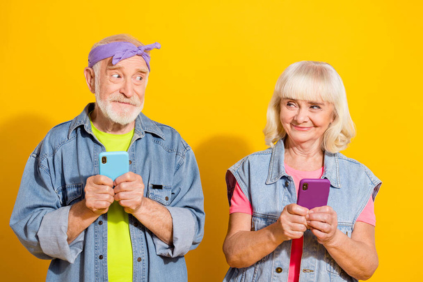 Photo of beautiful retired husband wife wear jeans clothes chatting modern devices isolated yellow color background - Φωτογραφία, εικόνα