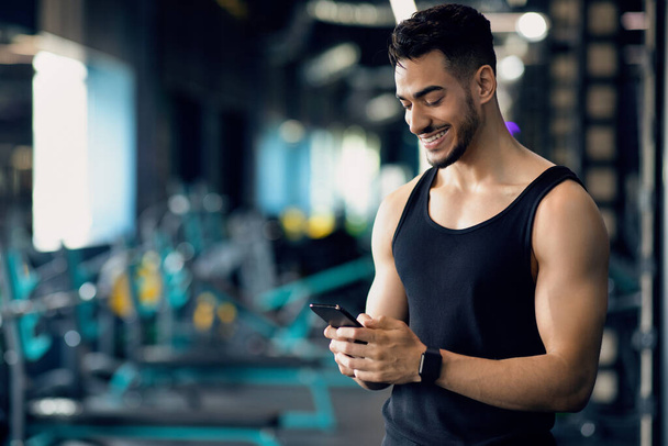 Fešák Mladý Blízký Východ Muž Použití Smartphone během tréninku ve sportovním klubu - Fotografie, Obrázek