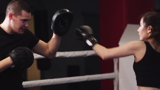 Młoda kobieta z długimi włosami trening boks z jej osobistym trenerem mężczyzn na ringu - uderzenie i unik - Materiał filmowy, wideo
