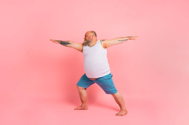 Funny man with beard in yoga position on studio pink background - Photo, Image