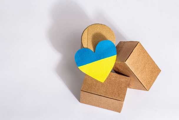 The concept of helping Ukraine in the war. Boxes with hearts in the colors of the Ukrainian flag isolated on a white background. Modern hard light, dark shadow - Photo, Image