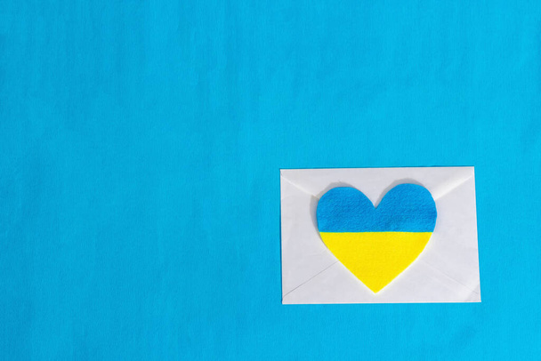 Envelope and heart in the colors of the Ukrainian flag. Stop the war concept isolated on blue background. Flat lay, a place for text, mockup, template, top view - Photo, Image
