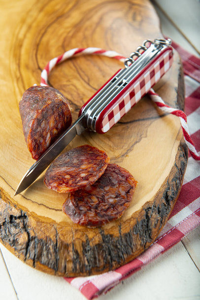 Couper le chorizo avec un couteau suisse sur une planche en bois et vichy habiller - Photo, image