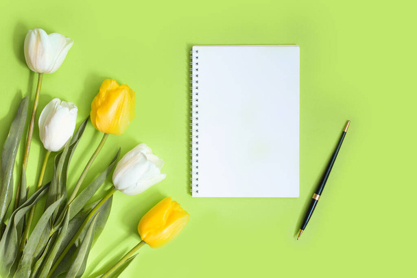 Composition with notebooks, stationery and yellow tulips on green background with space for text - Photo, Image