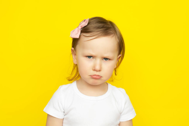 Little girl with sad expression on yellow background. - 写真・画像