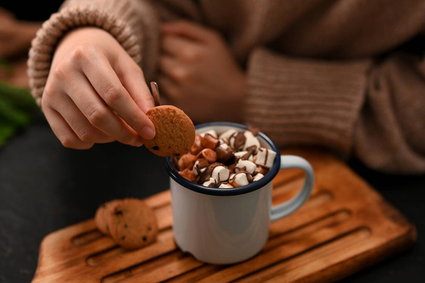Close-up, Focus hands, Female dripping soft cookie into a hot chocolate with marshmallows. Hot drink - Photo, Image