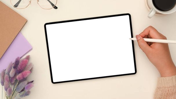 Boven schot, Vrouwelijke tekening op een digitaal tablet touchpad in haar stijlvolle werkruimte. Tablet wit scherm mockup. - Foto, afbeelding
