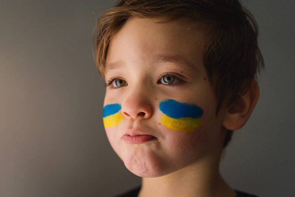 Portrait of a Ukrainian boy with a face painted with the colors of the Ukrainian flag. - Фото, изображение