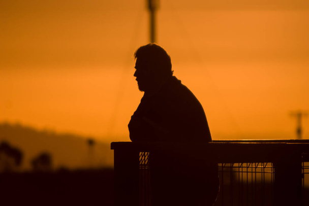 Silhouette eines Mannes mit Bart bei Sonnenuntergang an Zaun gelehnt mit Blick auf die Aussicht - Foto, Bild