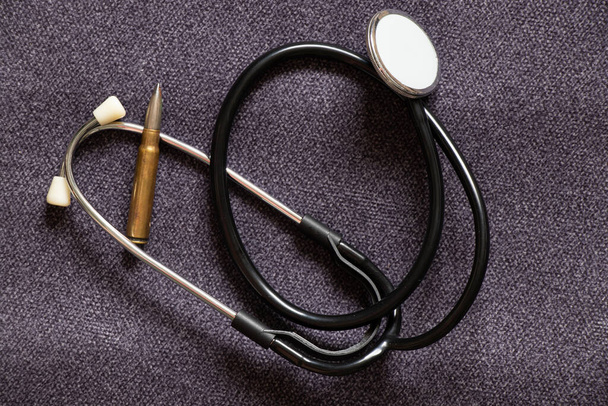 Stéthoscope d'un médecin et balle d'un soldat ledat sur fond gris, médecine militaire pendant la guerre en Ukraine, danger pour la santé - Photo, image