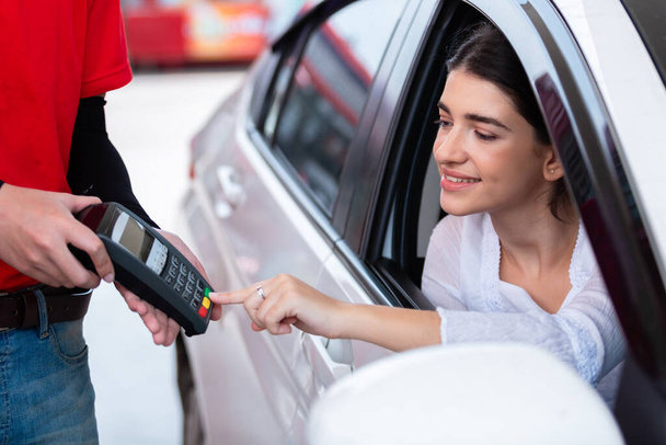 Woman in car paying card reader payment terminal after refuel car spending instead of cash with man service employee at gas station. - 写真・画像