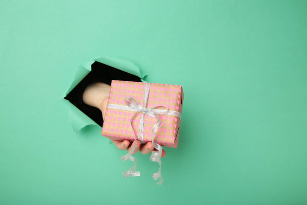 Female hand with gift box punching through the mint paper. Top view - Foto, afbeelding