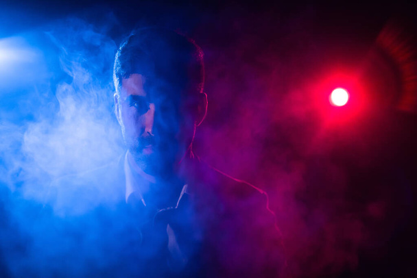 Photo of man looking at camera on dark background with pink and blue lights. - Φωτογραφία, εικόνα