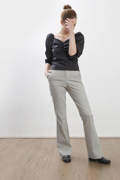Das weibliche Model trägt eine schwarze Bluse und eine schwarz-weiß gestreifte Hose. Studioaufnahme. - Foto, Bild