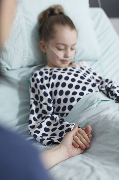 Junge Frau hält kranke Patientin im Krankenhaus an der Hand, während sie auf dem Bett der Kinderklinik liegt. - Foto, Bild