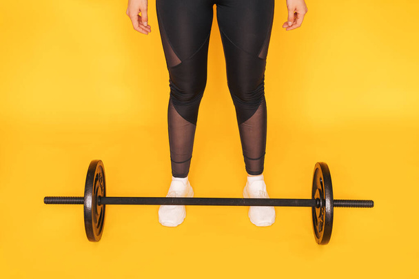The girl stands next to the barbell against yellow background - Φωτογραφία, εικόνα