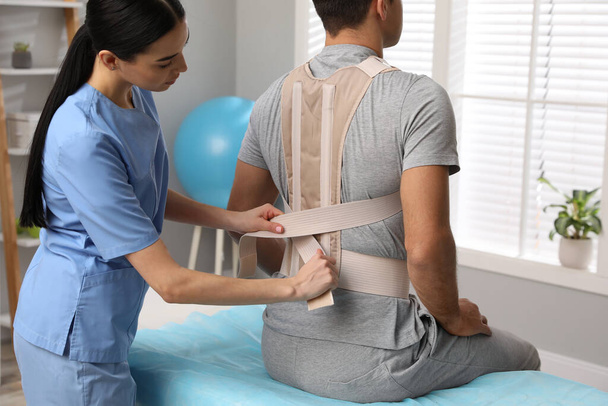 Orthopedist helping patient to put on posture corrector in clinic. Scoliosis treatment - Foto, Imagem