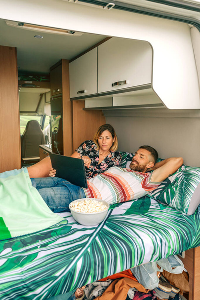 Paar liegt mit unordentlicher Kleidung und Schuhen unter dem Bett seines Wohnwagens und schaut sich einen Film an - Foto, Bild