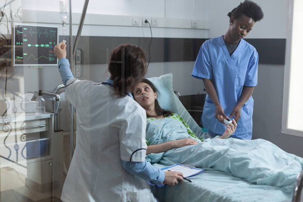 Pielęgniarka nakłada na palec pacjenta oksymetr pulsacyjny, podczas gdy lekarz ustawia kateter wkłucia centralnego - Zdjęcie, obraz