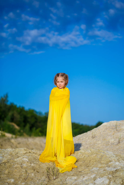 Oekraïense patriot meisje in een gele jurk tegen een blauwe lucht. Zomer foto. Blauwe lucht. Zonnige dag. Vrij Oekraïens kind. Kind symbool van Oekraïne - Foto, afbeelding