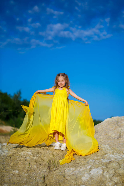 青い空に対して黄色のドレスのウクライナの愛国者の女の子。夏の写真。青い空だ。晴れた日。無料のウクライナの子供。ウクライナの子シンボル - 写真・画像