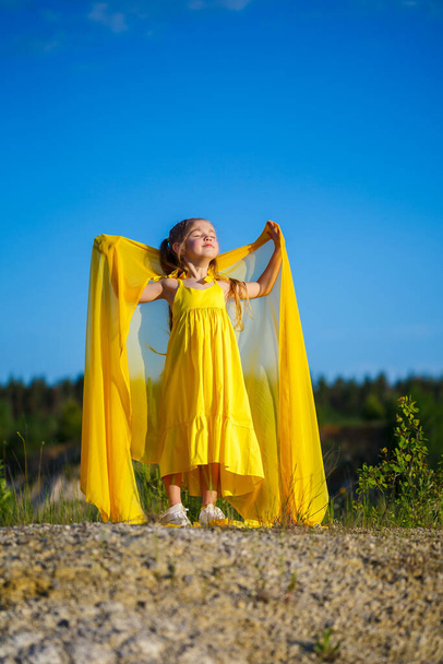自由のシンボルは、 7歳のウクライナの女の子で、愛国的に青い空に対して黄色のドレスを着ています。青い空だ。晴れた日。無料のウクライナの子供。ウクライナの子シンボル - 写真・画像