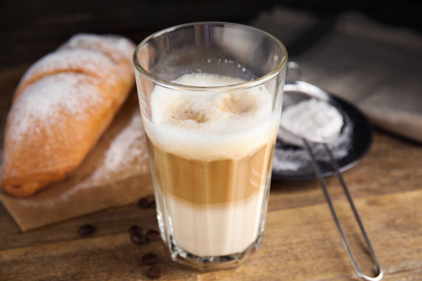 Delicious latte macchiato, croissant and scattered coffee beans on wooden table - Foto, imagen