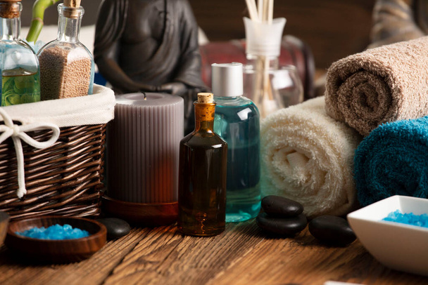 Spa and wellness concept. Bottles with cosmetics, rolled up towels, bath salts and care products on wooden paneling. - Photo, Image