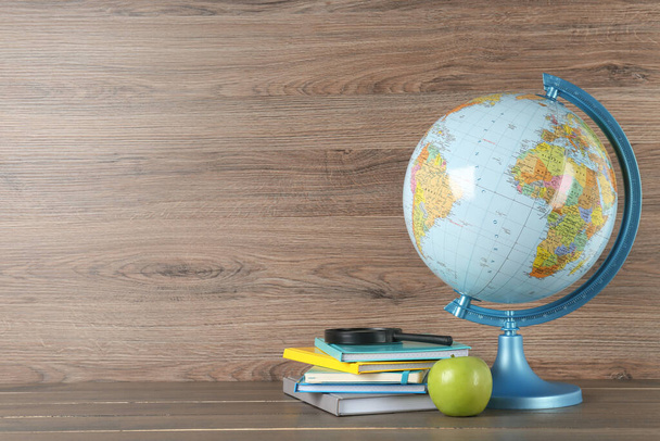 Globe, books, magnifying glass and apple on wooden table, space for text. Geography lesson - Φωτογραφία, εικόνα