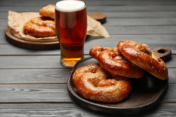 Tasty freshly baked pretzels and glass of beer on grey wooden table. Space for text - Foto, Bild