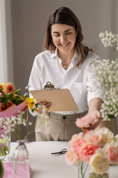 happy woman with clipboard and flowers at studio - Fotó, kép
