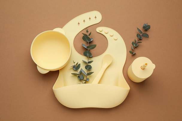 Flat lay composition with baby feeding accessories and bib on brown background - Фото, зображення