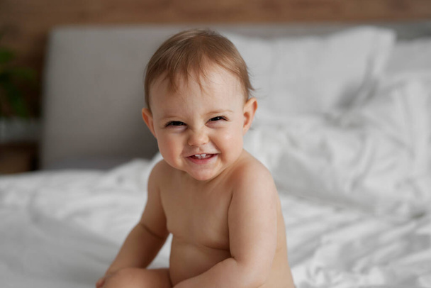 Сміється біла дівчинка після ванни, що сидить на ліжку
  - Фото, зображення