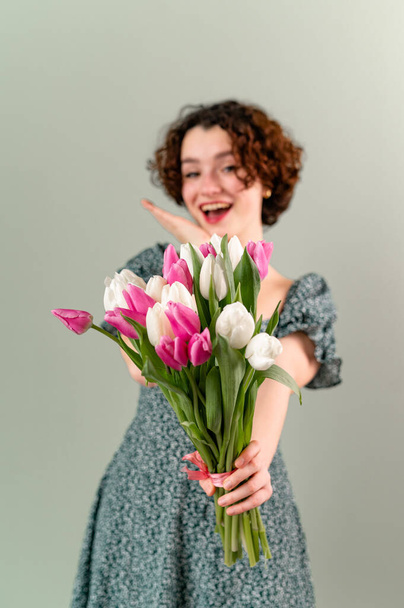 Krásná teenager dívka s kudrlinkami na šedém pozadí drží kytici tulipánů. Selektivní zaměření - Fotografie, Obrázek