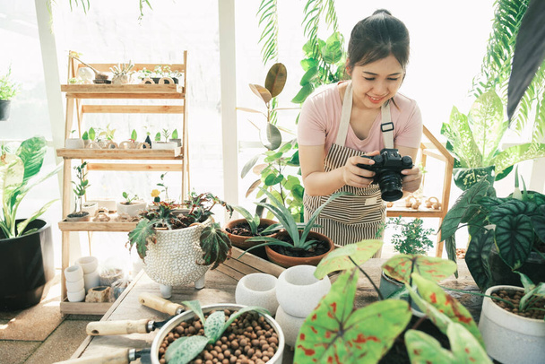Sorrindo jovem mulher tirando foto smartphone da planta em uma pequena loja - Foto, Imagem