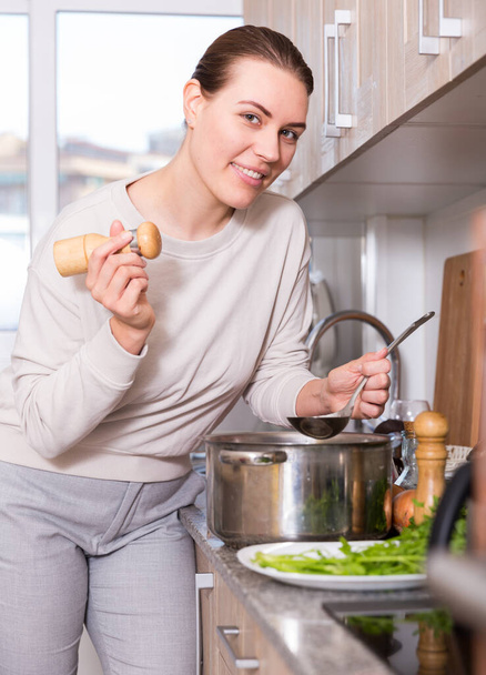 Young woman is cooking soup and salt it in the kitchen - Φωτογραφία, εικόνα