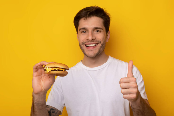 Смішний хлопець тримає бургери показуючи великий палець вгору
 - Фото, зображення