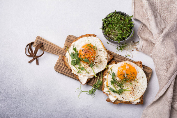 Top view of sandwich with fried eggs, toasts, alfalfa and green pea sprouts microgreen for breakfast on grey concrete background - Foto, imagen