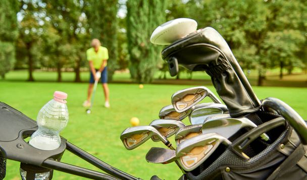 ゴルフコースでゴルファー、ティーオフする準備ができています。完璧なショットのためにボールを打つゴルフクラブとゴルファー.前景では、バッグやゴルフクラブとゴルフカート - 写真・画像