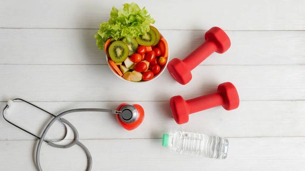 Health Care.  Fresh vegetable salad with medical stethoscope and equipment dumbbell for diet and weight loss for healthy care and protect virus,  white wooden background.  Healthy Life Concept - Foto, Imagen