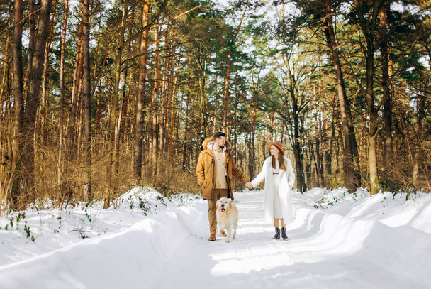 Kaukázusi pár a szabadban. Romantikus bájos lány és brutális férfi a téli erdőben, akik szabadidejüket töltik retriever kutyával. Szezon, szerelem, család, szépség. - Fotó, kép